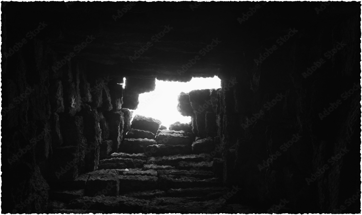 black and white of a brick wall with a few bricks missing at the center with light shining through